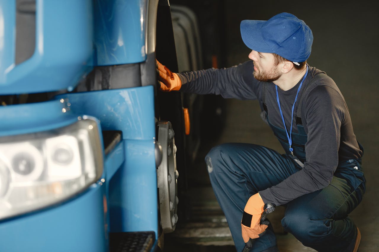 services-02 Mechanic in uniform checking a blue truck's wheel inside a garage workshop.