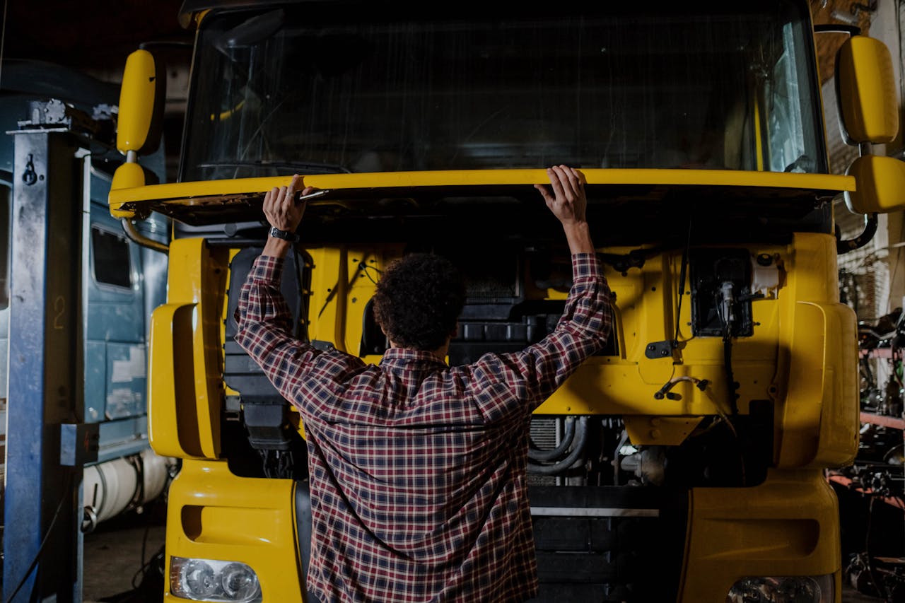 services-01 Rear view of a mechanic inspecting a yellow truck engine in a garage setting.